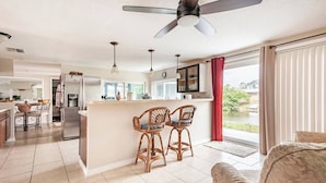 A spacious living area with a large window, a ceiling fan, and a kitchen in the background. - Private bedroom and private bath at separate end of home with water views. (New Port Richey)