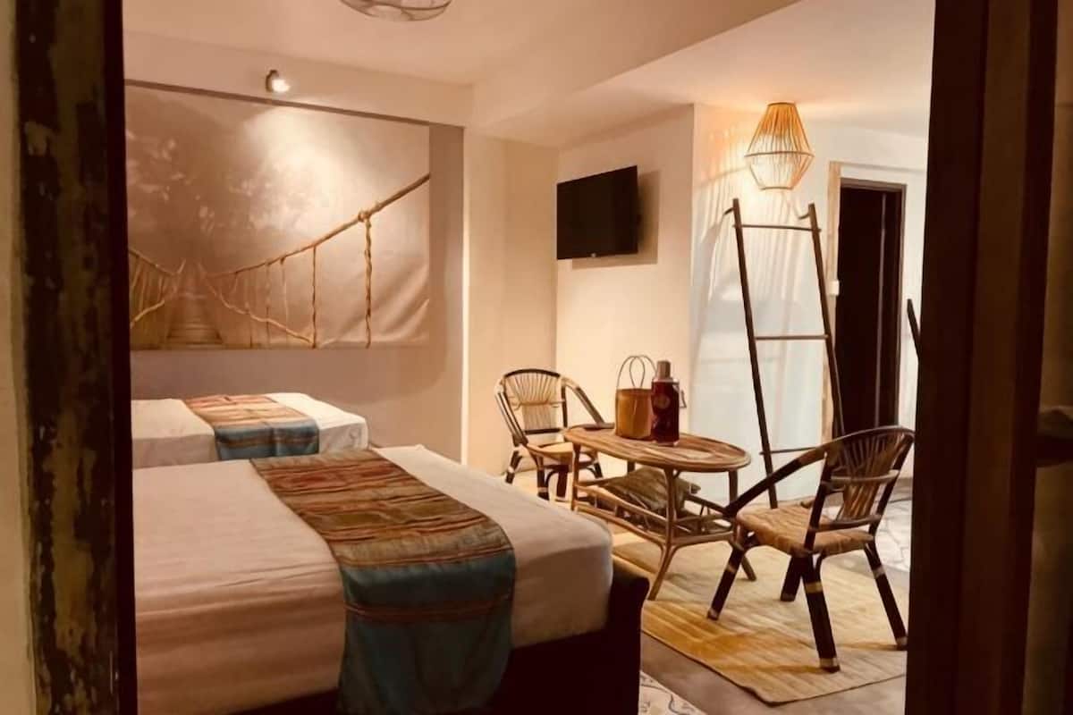A hotel room with two beds, a television, a table with chairs, and a hanging chair.