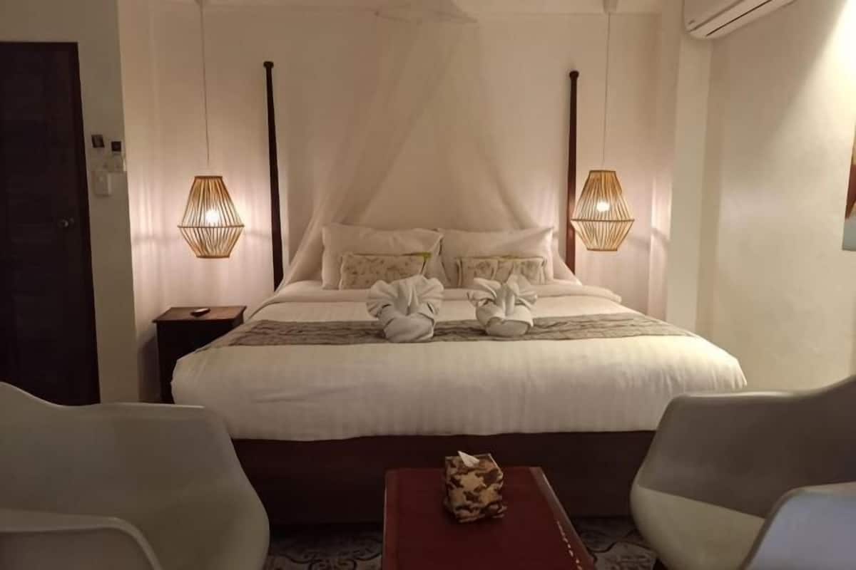 A hotel room with a large bed, two bedside lamps, a bedside table, and two chairs.