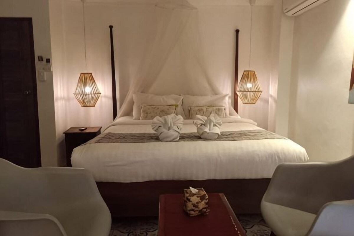 Una habitación de hotel con una cama grande, dos l ámparas de noche, una mesita de noche y dos sillas.