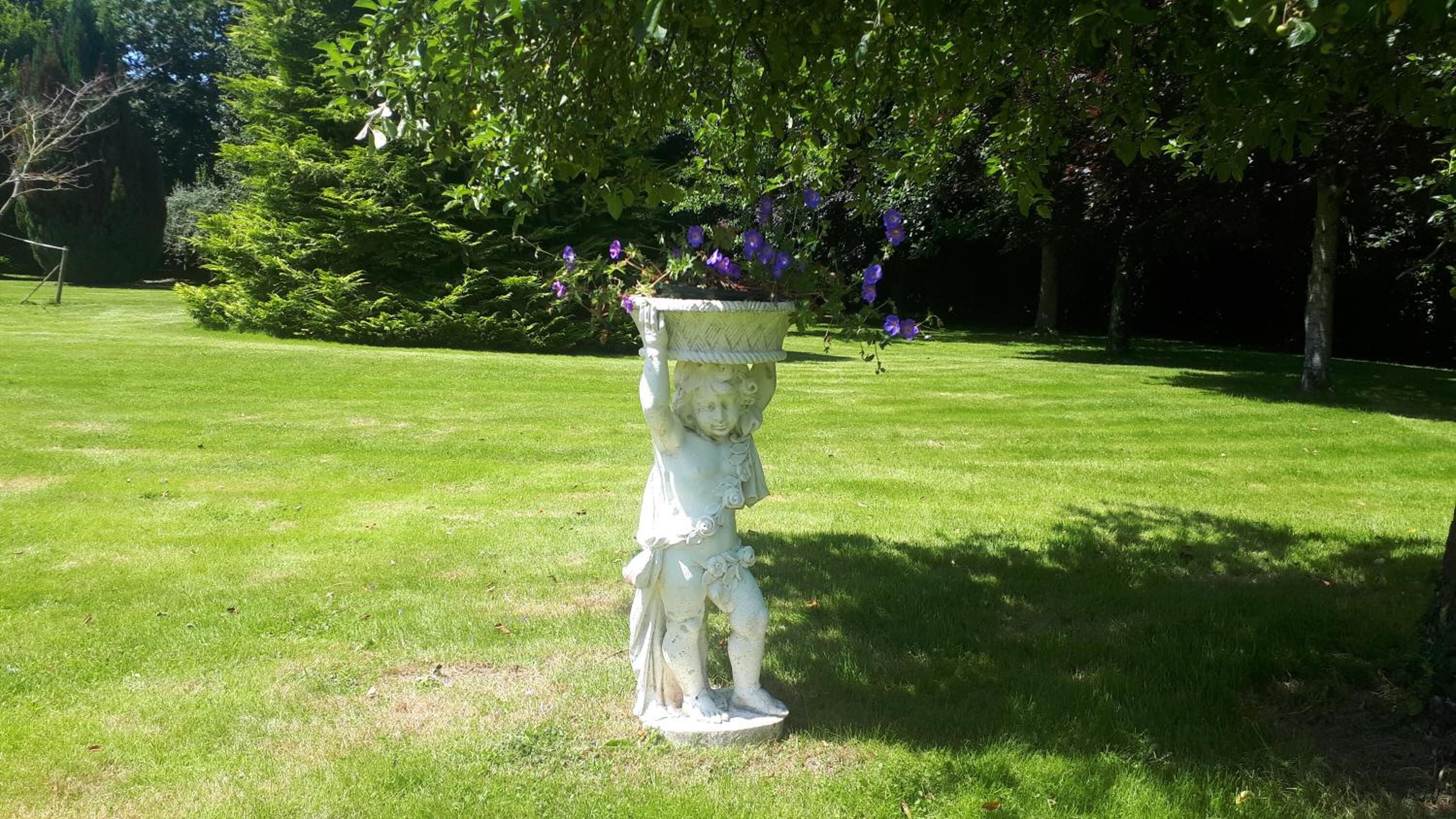 Eine Gartenstatue mit einem Pflanzgefäß auf einer grünen Rasenfläche.