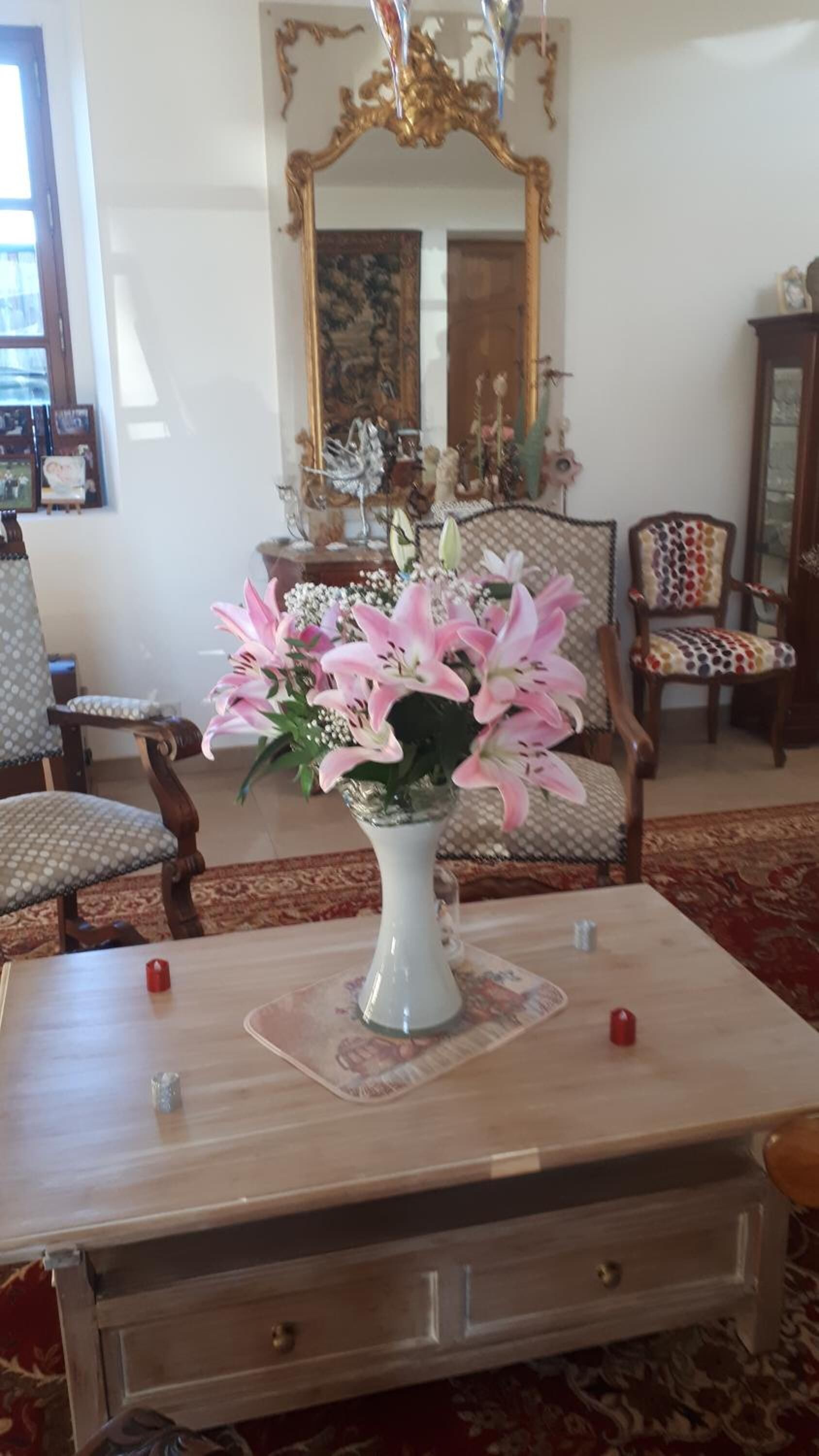 A room with a wooden table, a vase of flowers, and a mirror on the wall.