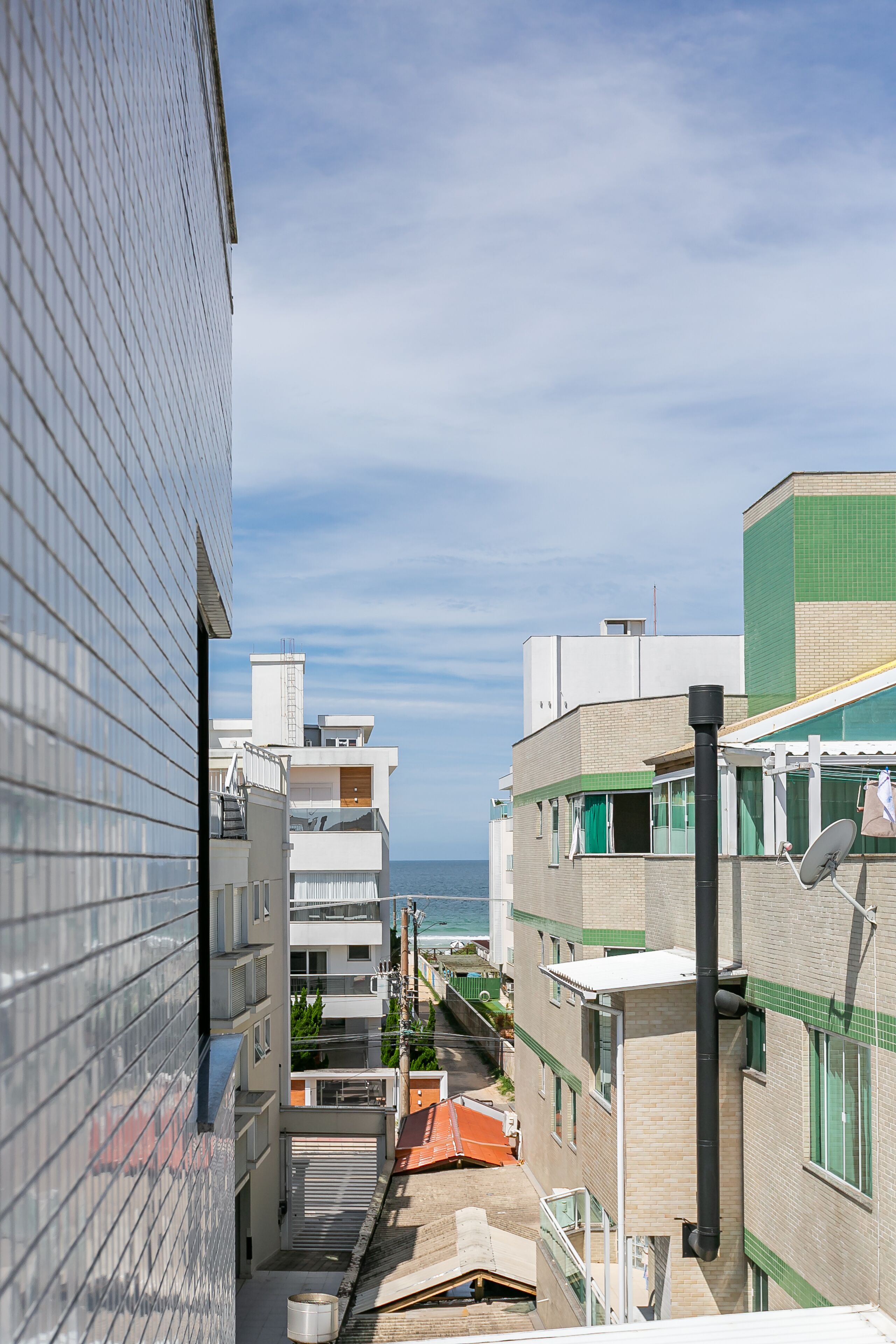 A narrow urban street with buildings on both sides, a clear sky, and a view of the sea in the distance.