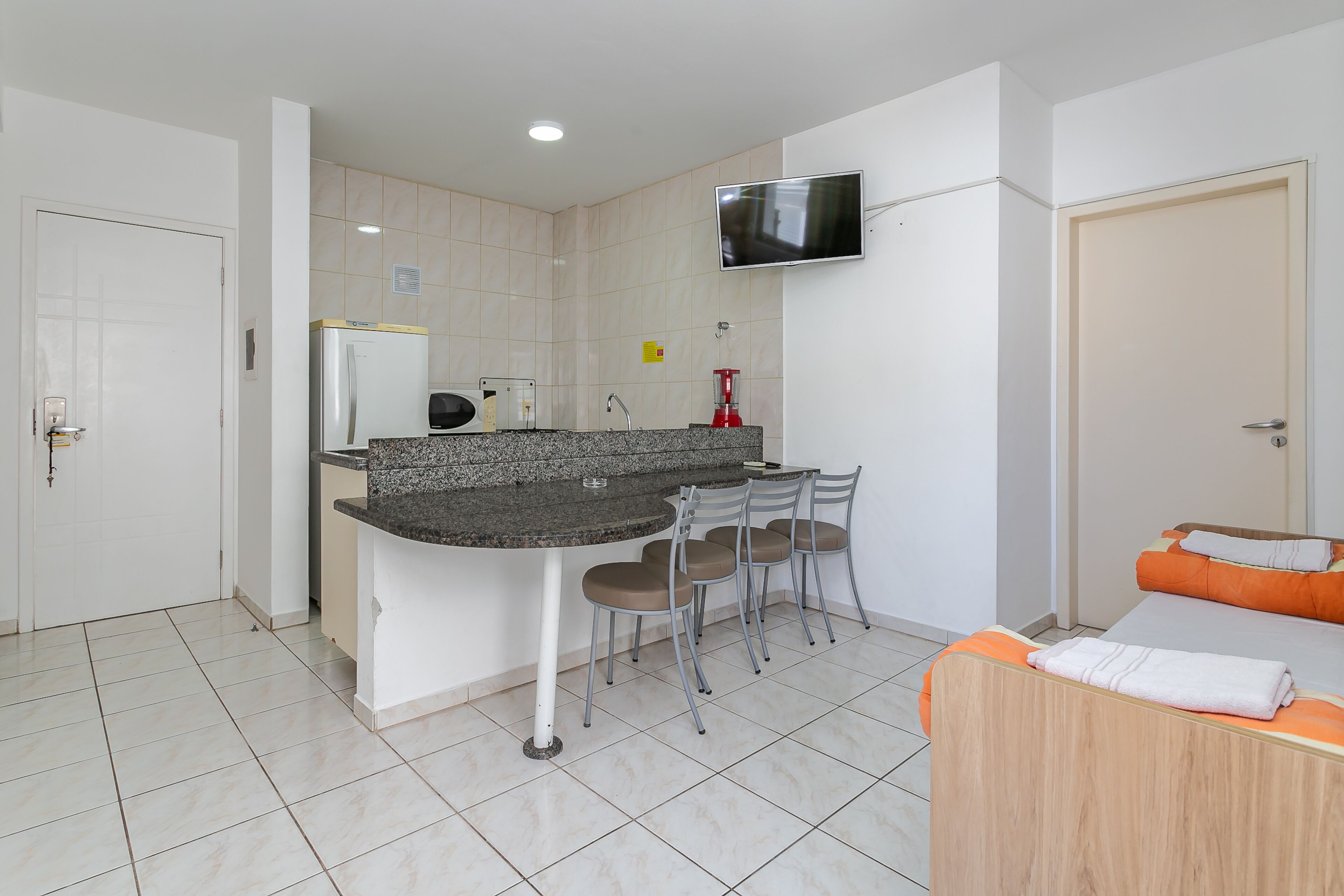 A compact kitchen with a built-in microwave, a refrigerator, and a flat-screen TV mounted on the wall.
