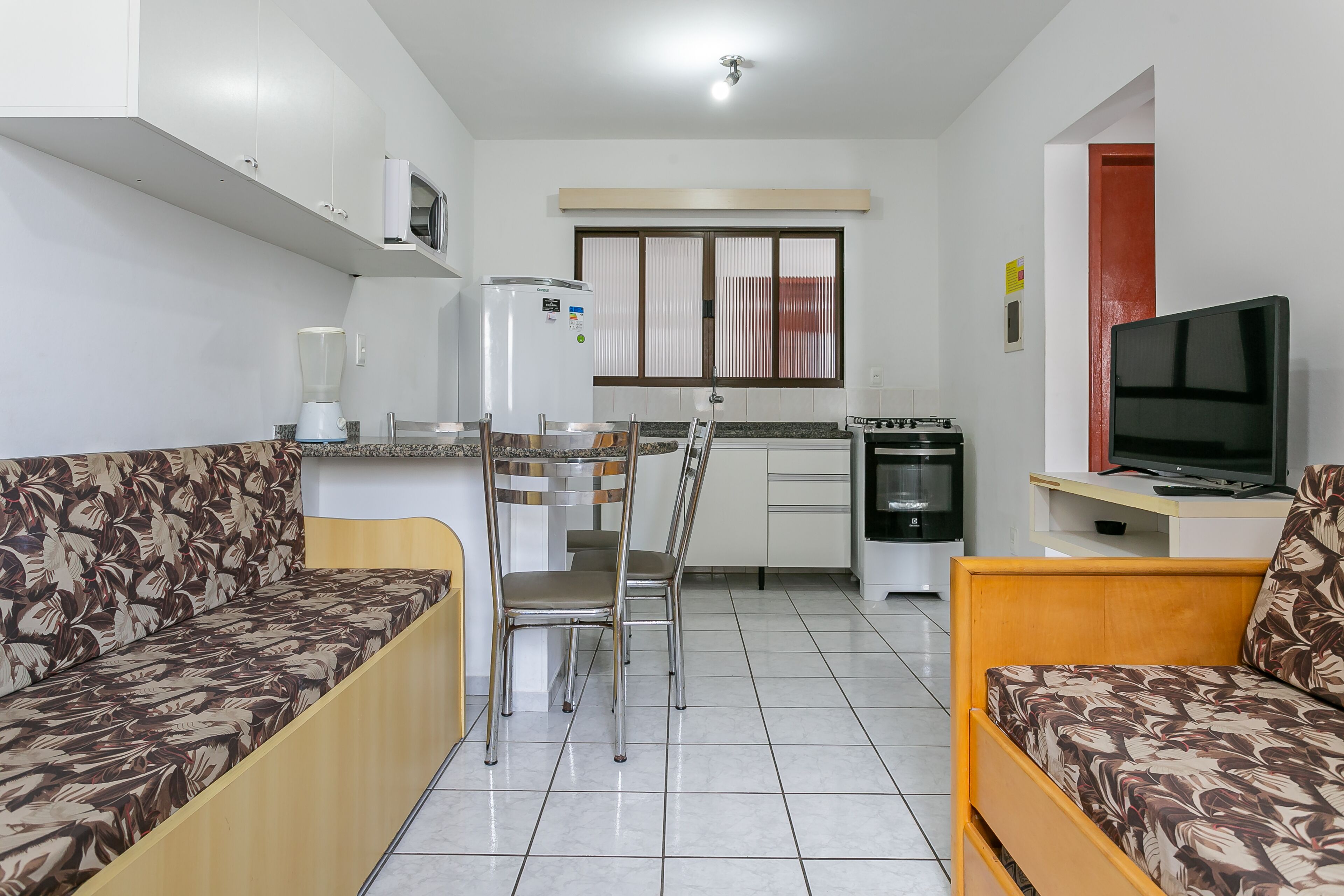 A compact living space with a kitchenette, a sofa, a dining table, and a TV.