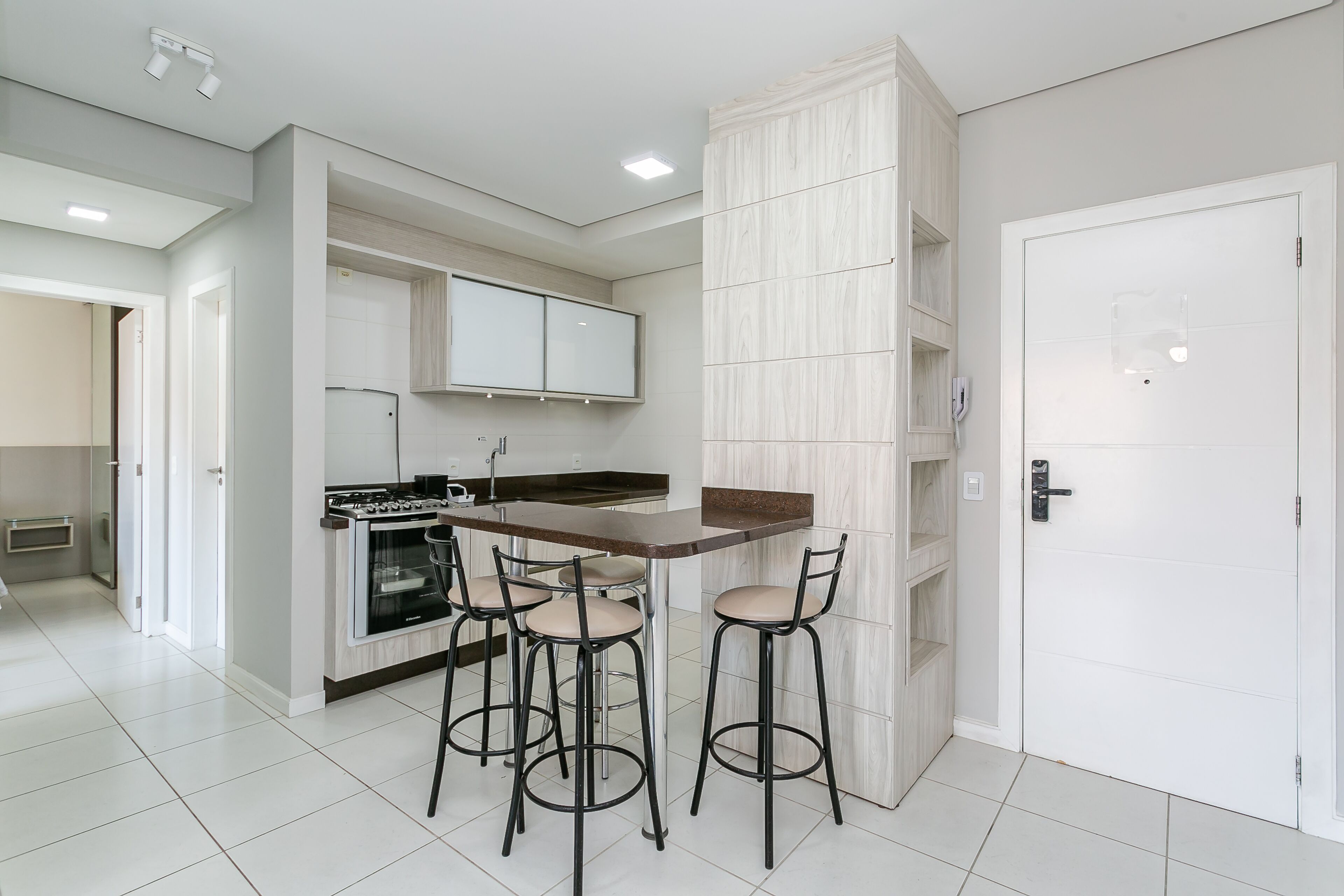 Una cocina moderna con una isla central, taburetes de bar y una puerta blanca.