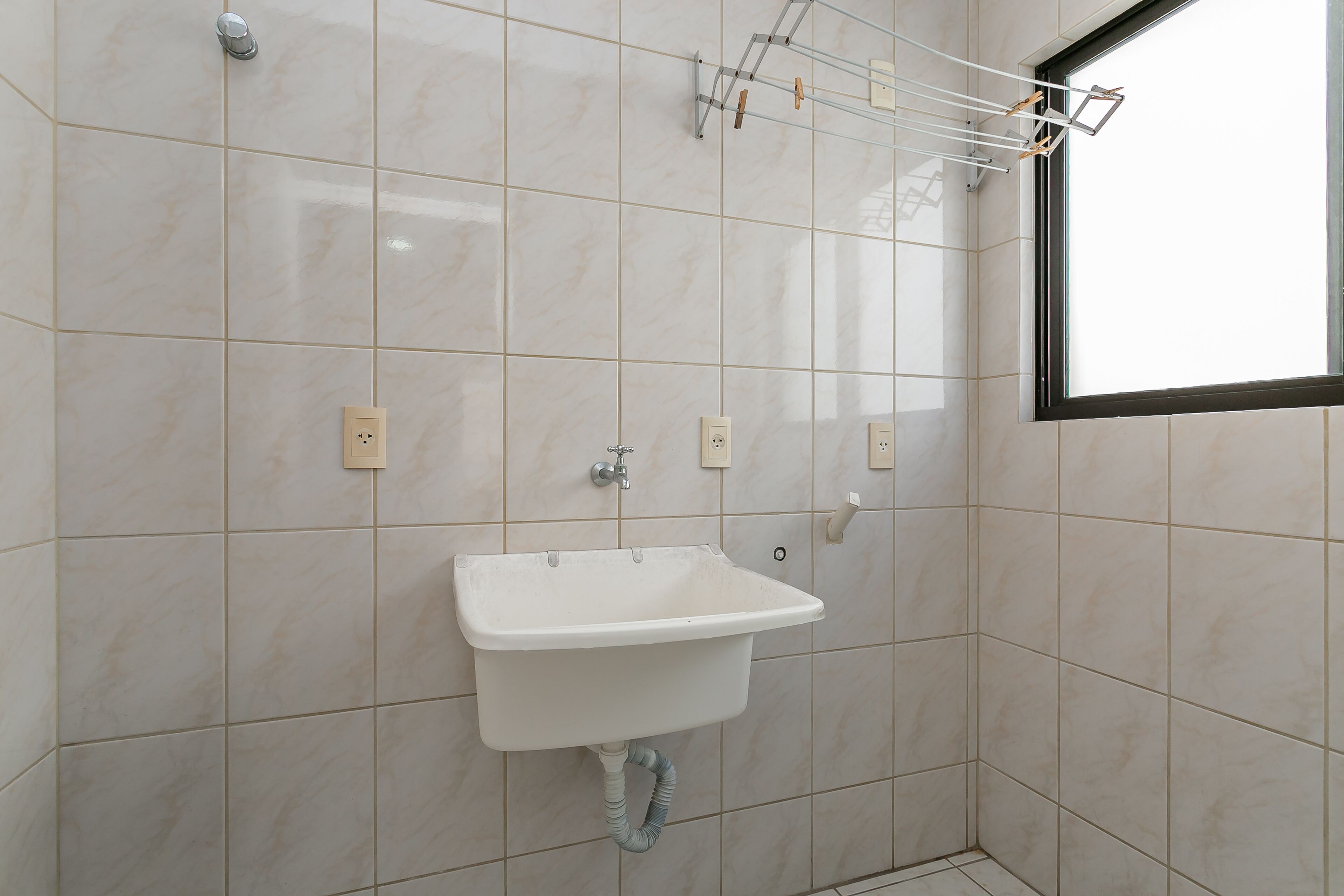 Un baño con un lavamanos blanco, paredes con azulejos, una ventana y un perchero para toallas.