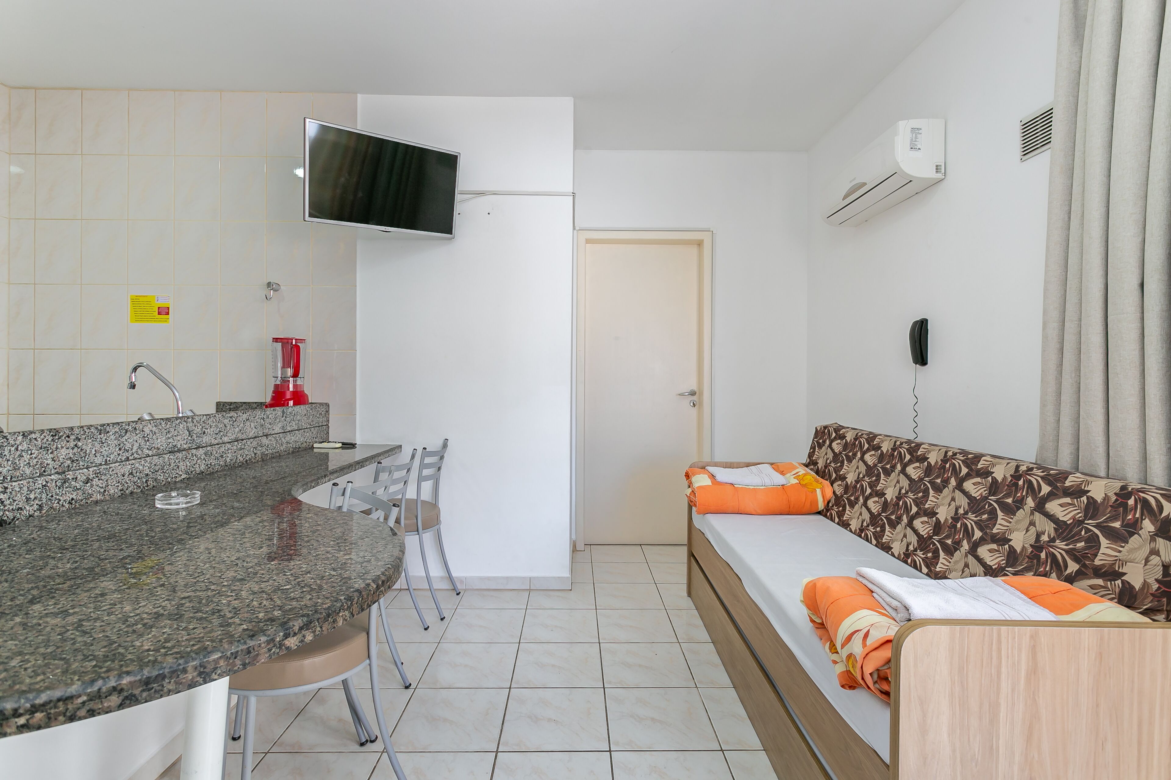Een kleine kamer met een kitchenette, een bank, een televisie en een telefoon.