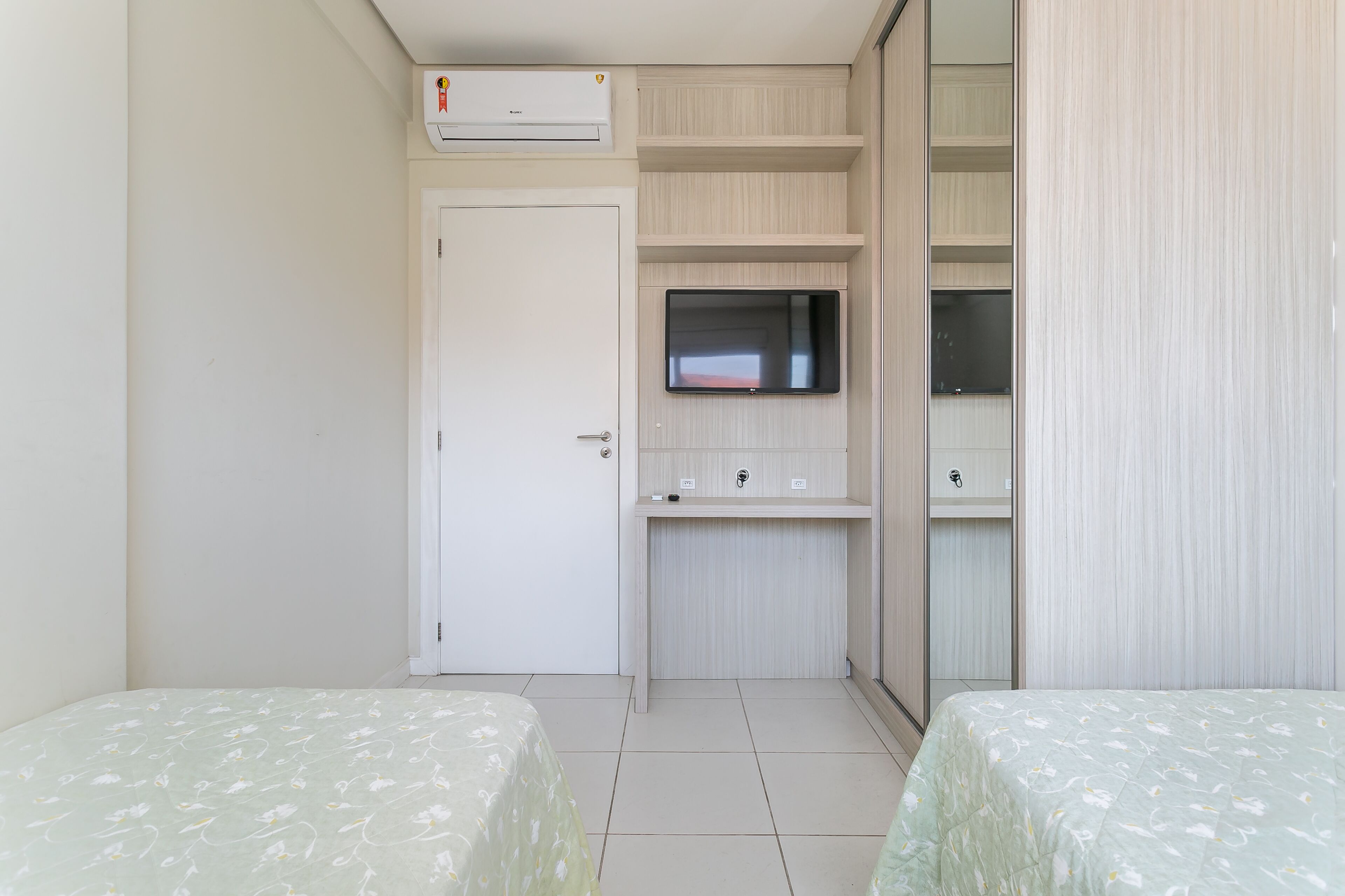 A small, clean room with two beds, a TV, a wardrobe, and a desk.