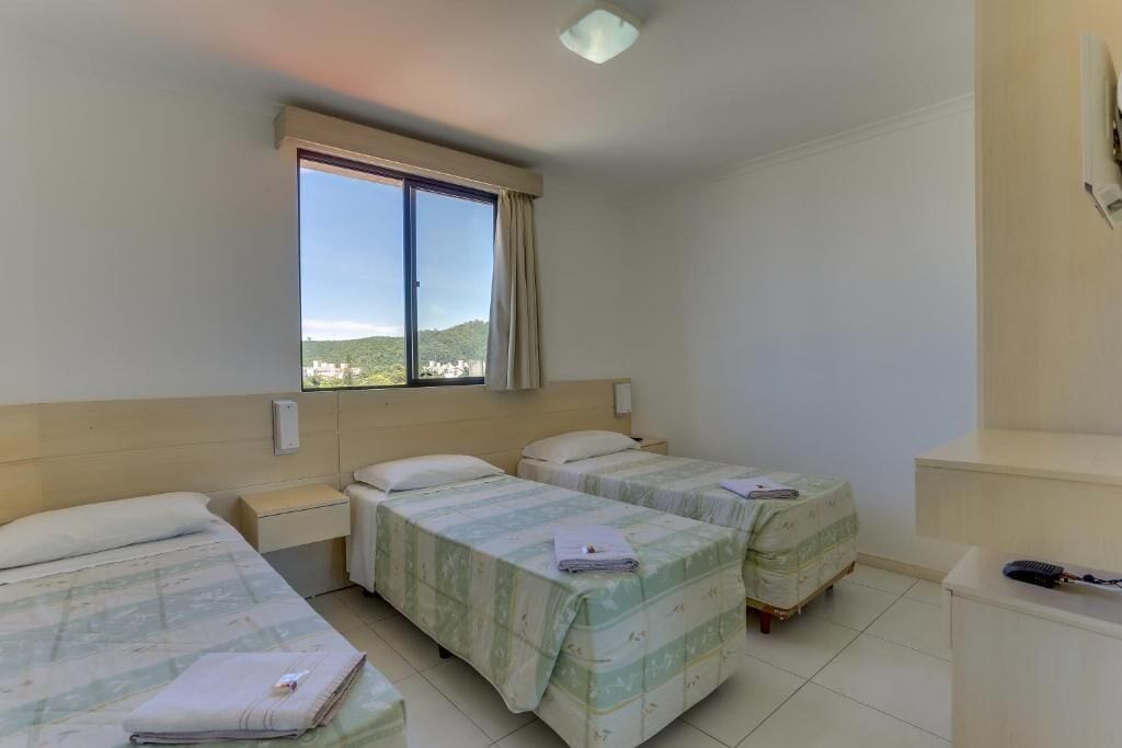 Habitación de hotel con dos camas, un escritorio pequeño y una ventana que ofrece vistas a una colina.