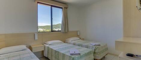 Habitación de hotel con dos camas, un escritorio pequeño y una ventana que ofrece vistas a una colina.