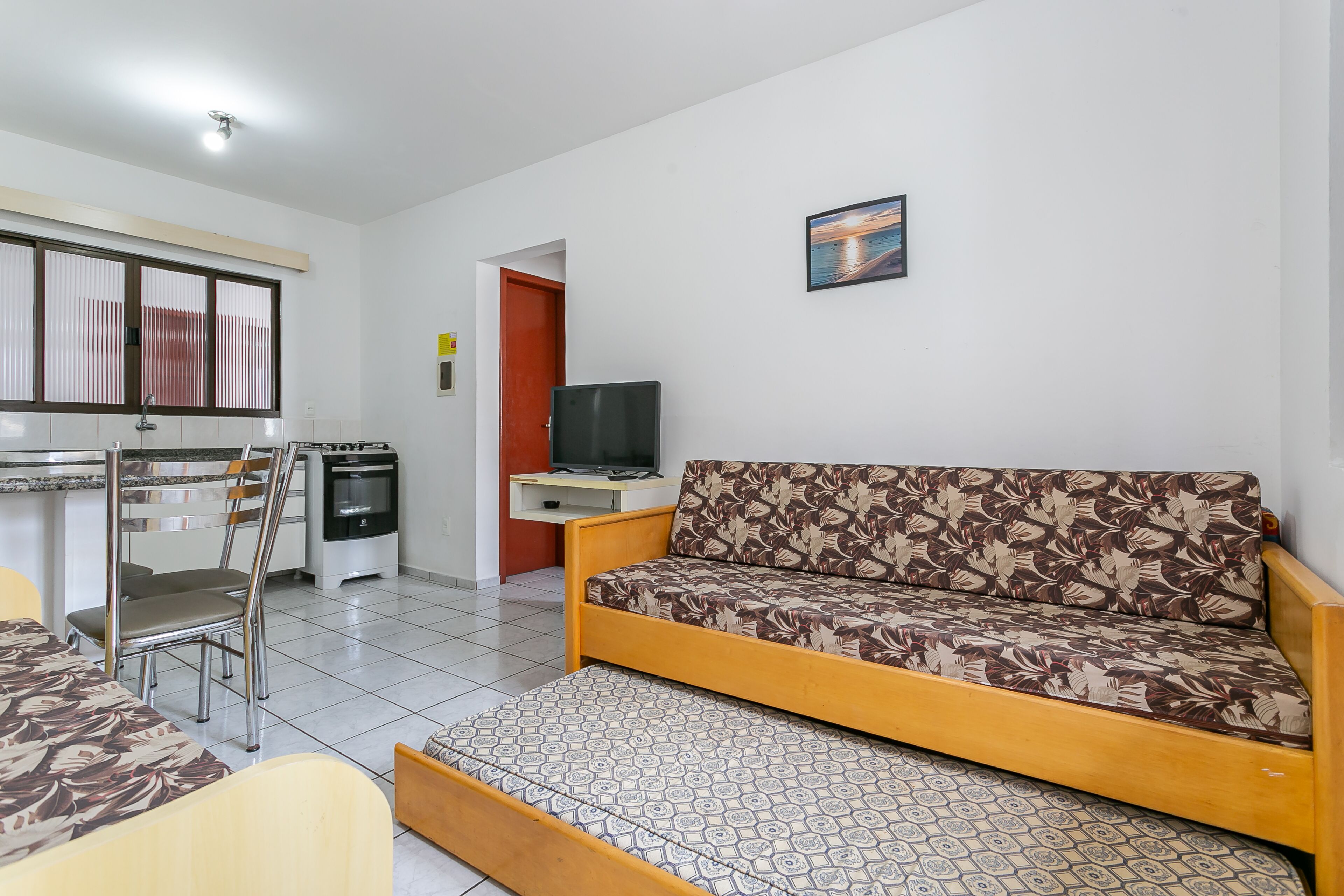 Un espacio habitable compacto con sofá, mesa de comedor con sillas, kitchenette y televisor.