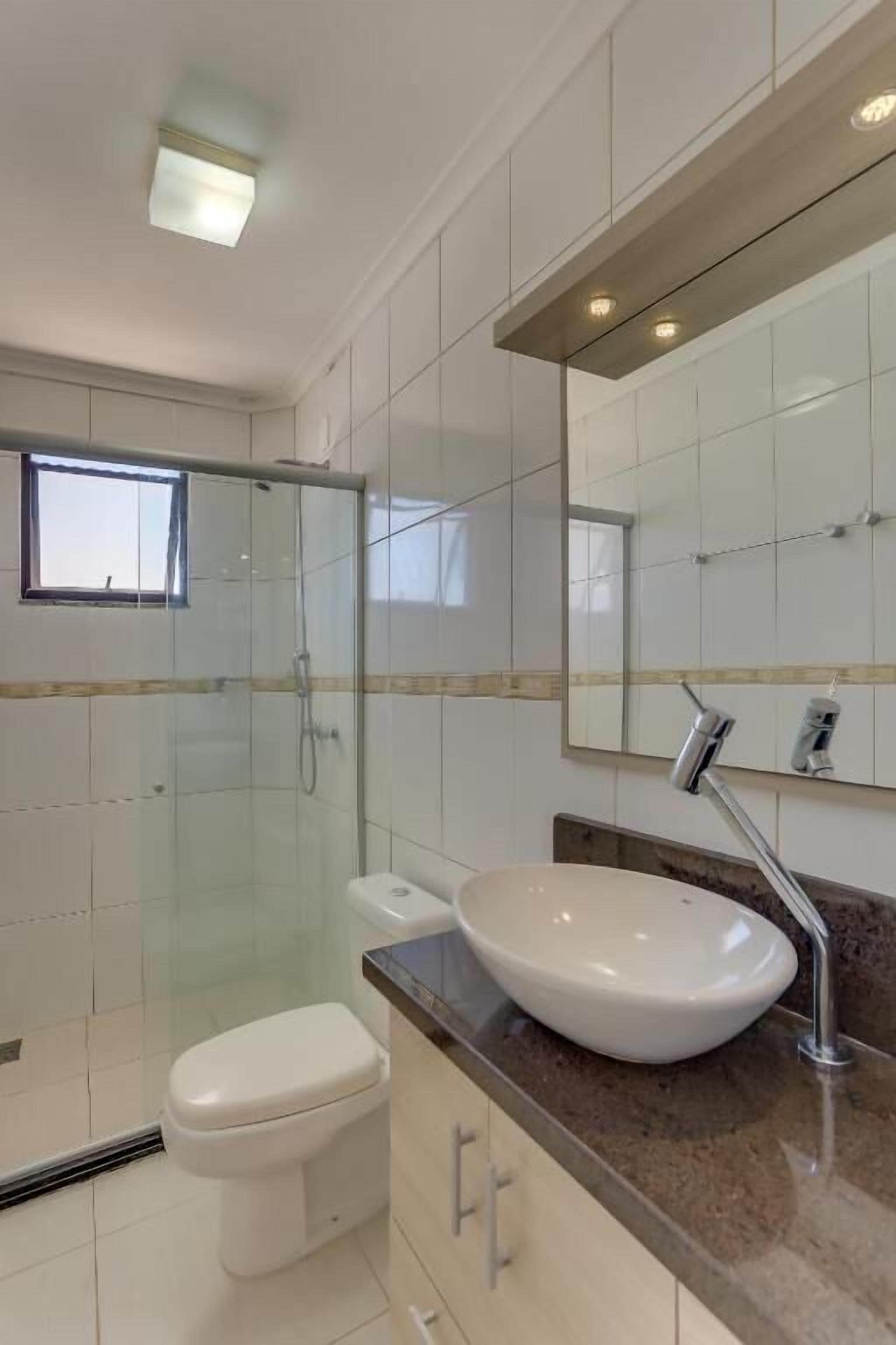 A modern bathroom with a glass-enclosed shower, a white toilet, and a large mirror above a sink with a vessel basin.