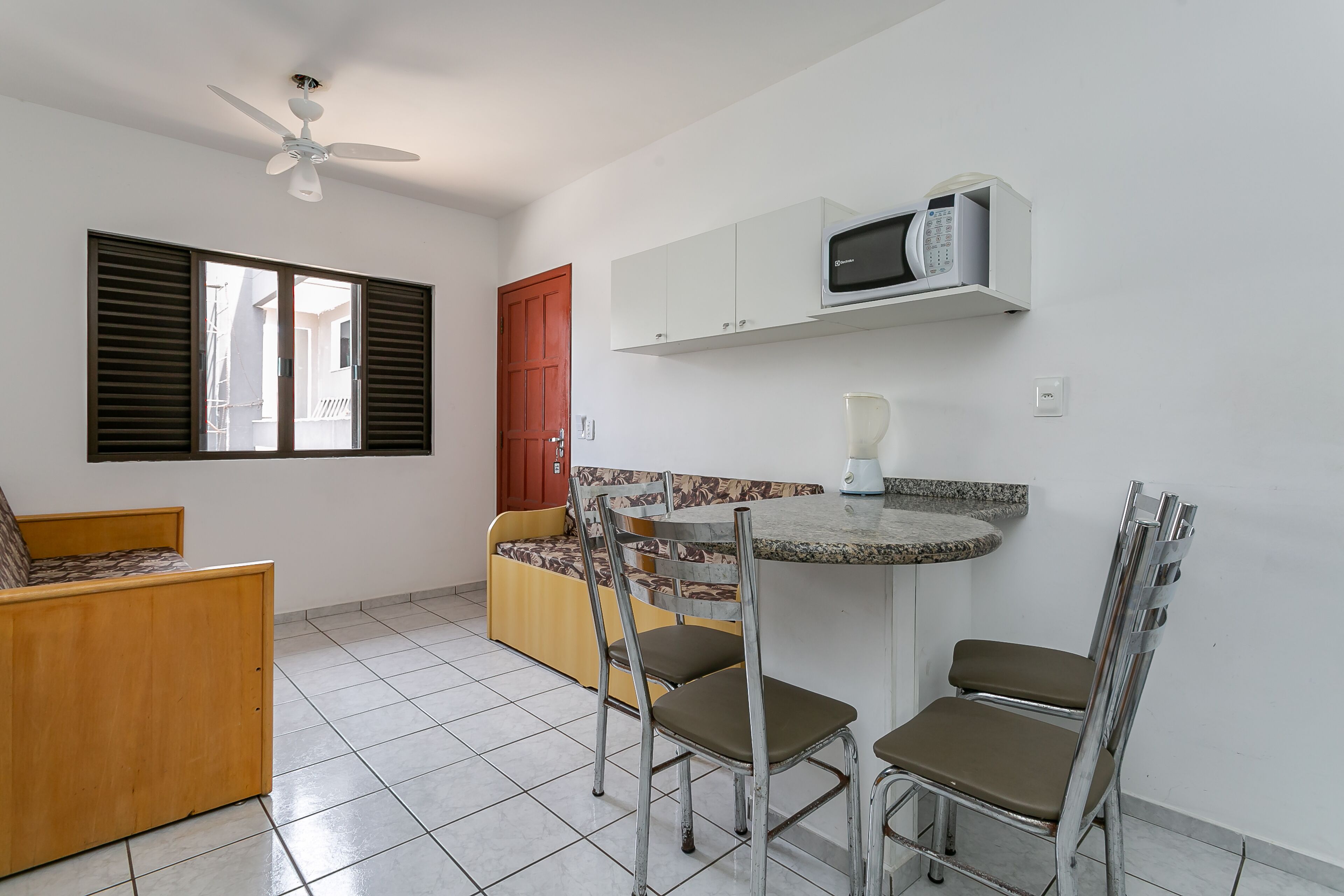 A compact kitchen with a microwave, a blender, and a dining area with chairs and a small table.