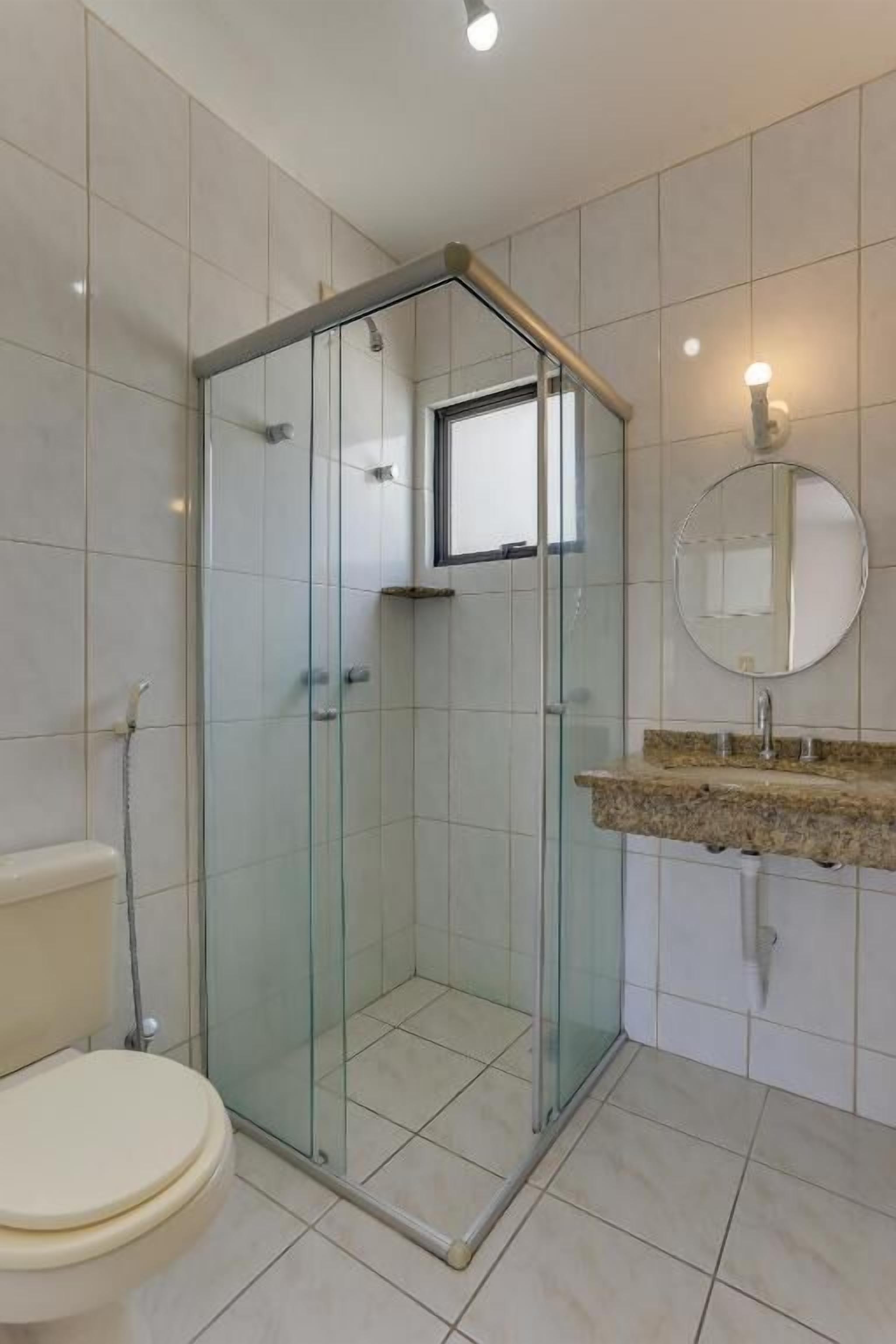 A modern bathroom with a glass-enclosed shower, a toilet, and a sink with a granite countertop.