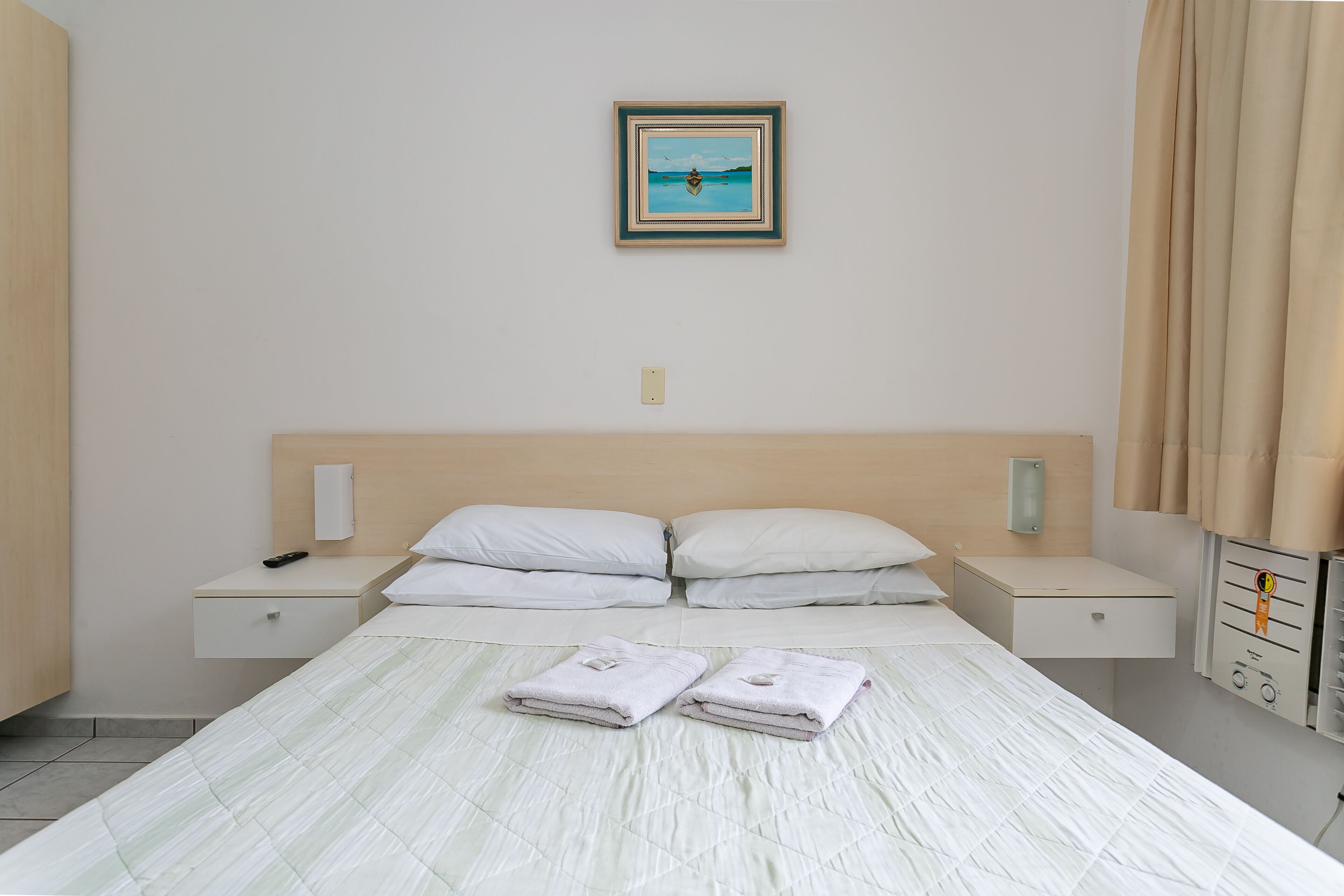 Habitación de hotel con cama, dos mesitas de noche, lámpara de pared, toma de corriente y termostato.