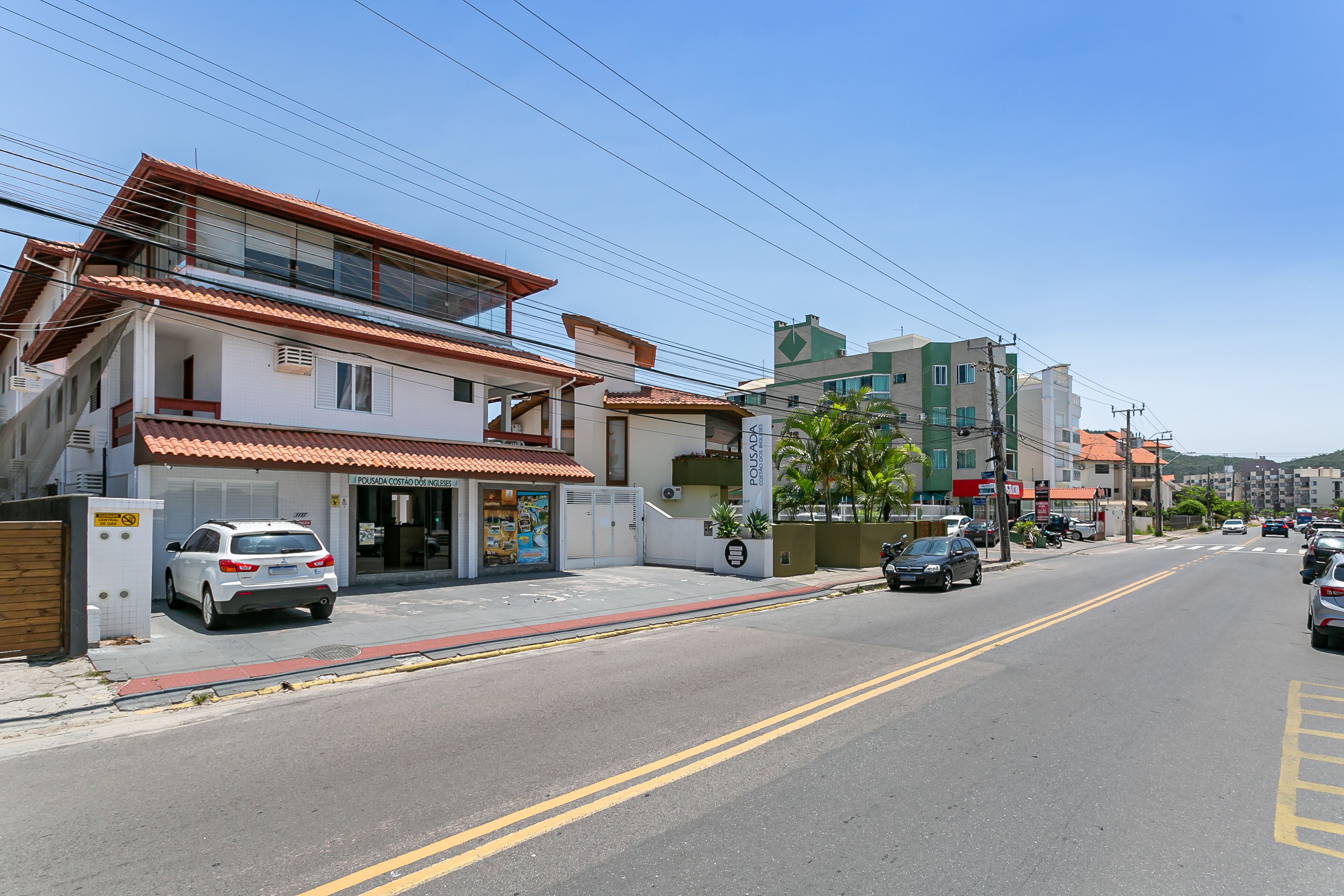 A street view with buildings, a white car parked on the side, and a clear blue sky.