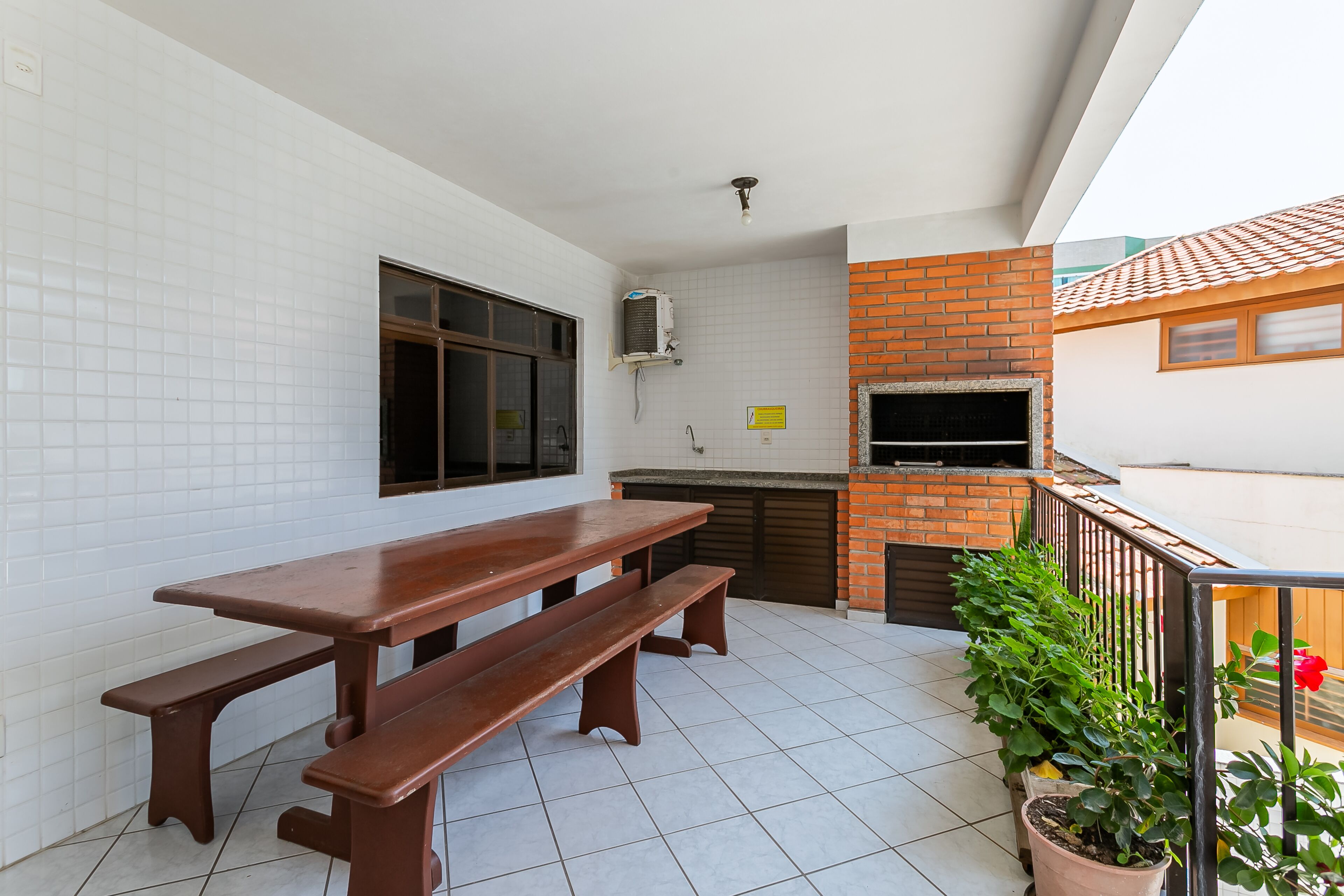 Um pátio com mesa e bancos de madeira, forno de tijolos e plantas em vasos.