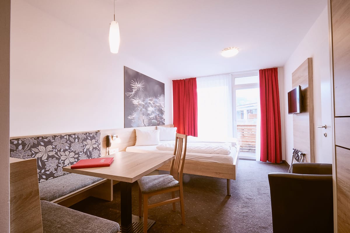 A room with a bed, a desk, a chair, a table, and a TV.