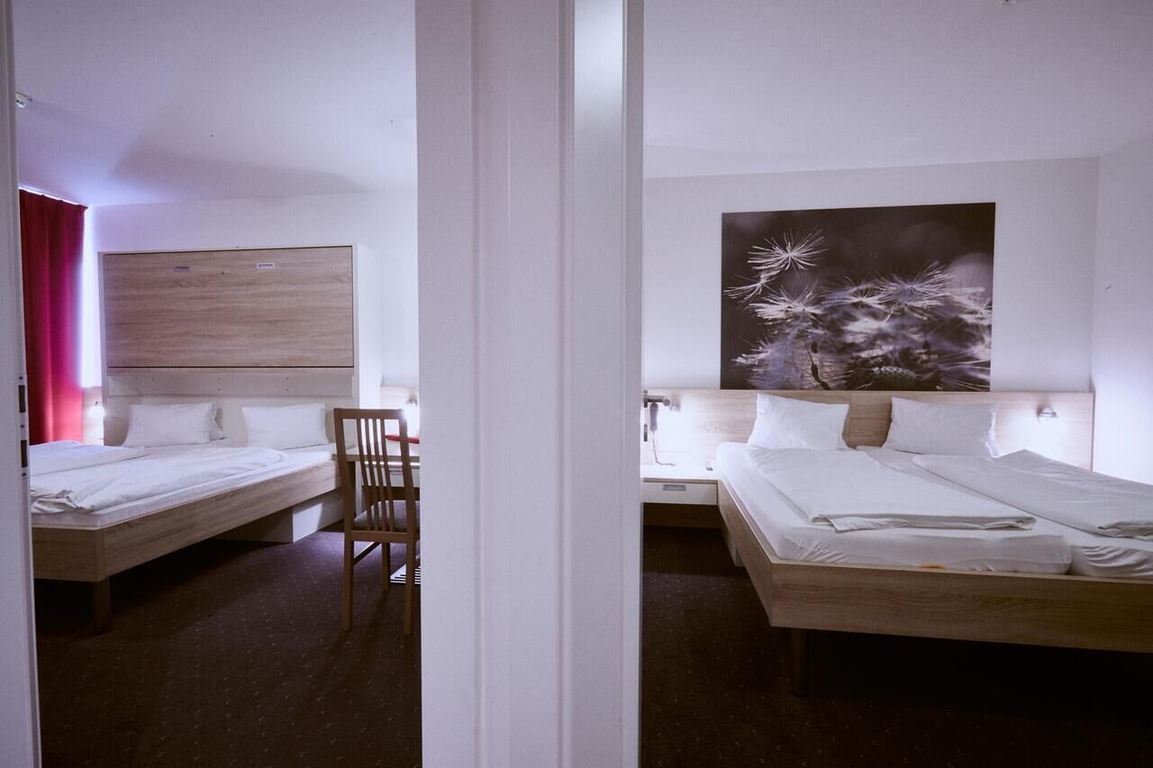 Habitación de hotel con dos camas individuales, cabecero de madera, una silla y un cuadro abstracto grande en la pared.