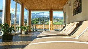 A sunlit room with large windows, wooden beams, and lounge chairs facing a scenic mountain view. - Hotel Planai by Alpeffect Hotels (Schladming)