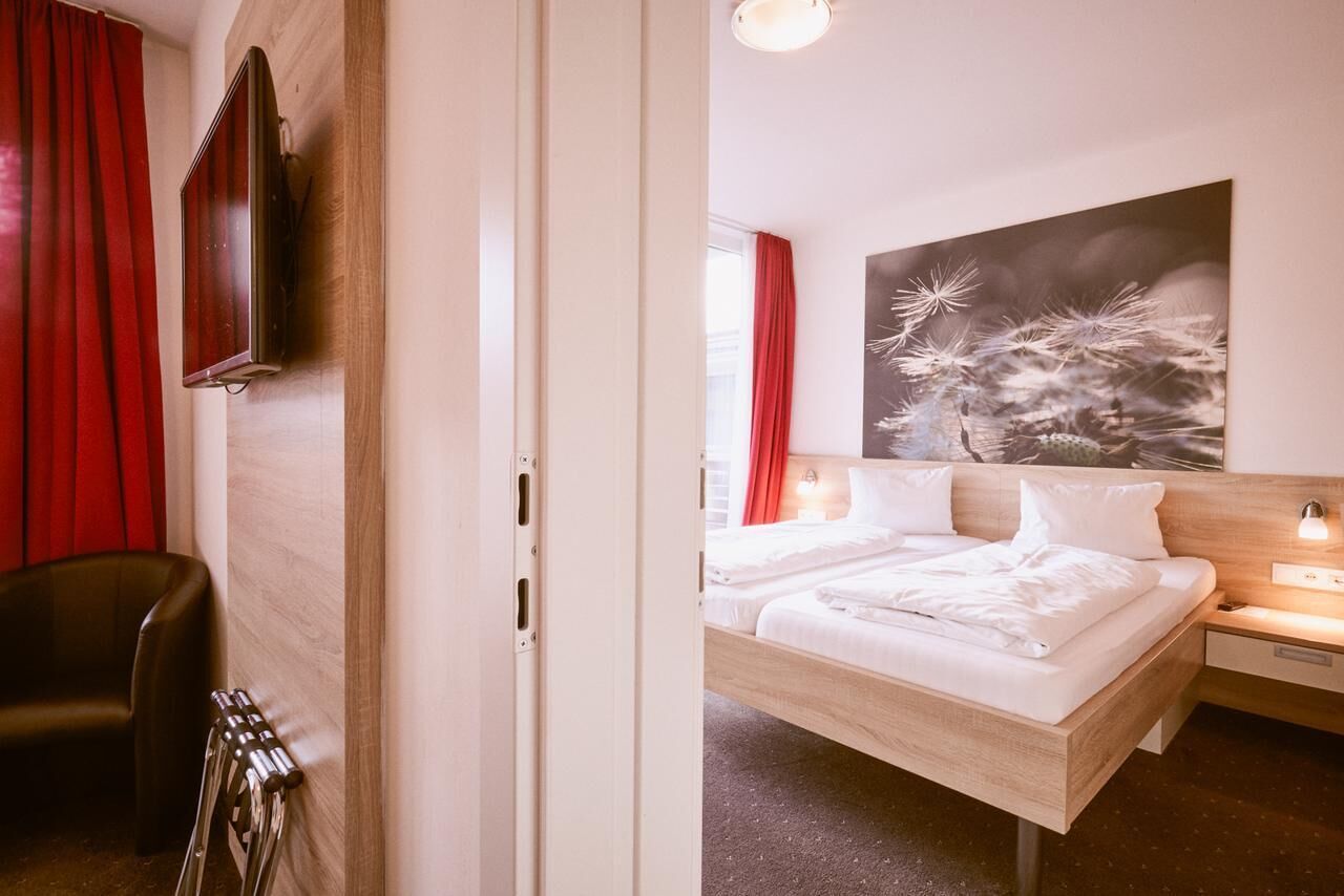 A hotel room with a bed, a chair, a TV mounted on the wall, and a painting above the bed.