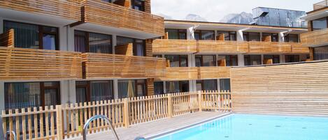 Un hotel moderno con varios balcones, piscina y vistas a las montañas.