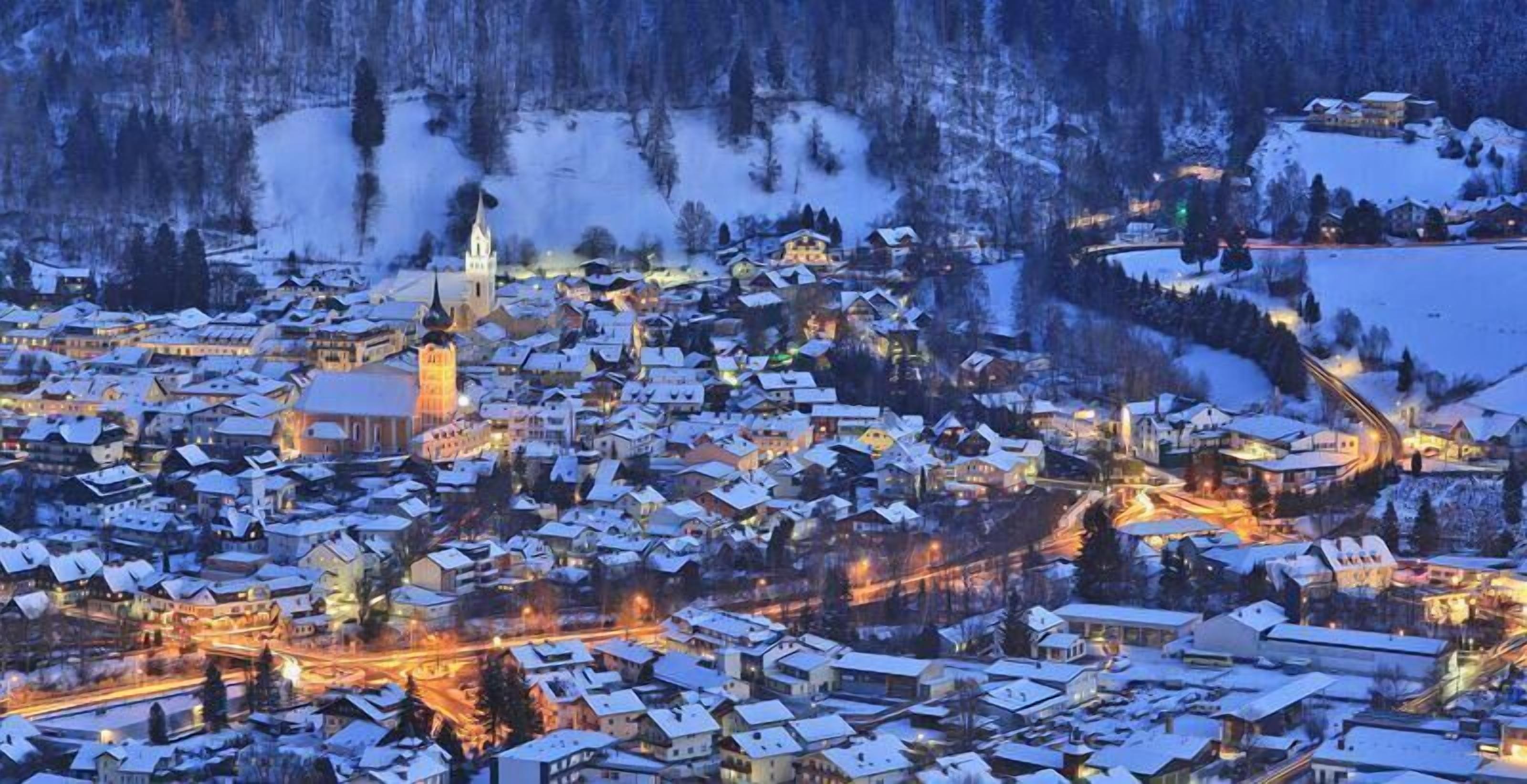 A snow-covered town with illuminated buildings and a prominent church tower.