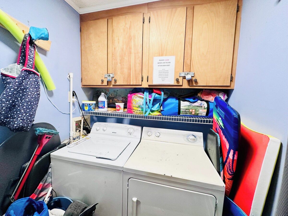 A laundry area with a washing machine, a cabinet with a cleaning notice, and various cleaning supplies.