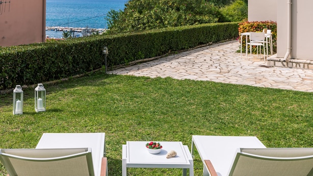 A patio with two white chairs, a small table with a bowl of fruit, and a view of the sea and mountains in the background. - Seaview Luxurious Apartment near Corfu Town - Adults Only By Konnect (Corfu)