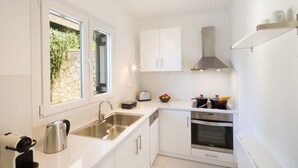 A modern kitchen with white cabinetry, a stainless steel sink, a built-in oven, and a window with a stone wall view. - Seaview Luxurious Apartment near Corfu Town - Adults Only By Konnect (Corfu)
