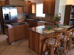 Enjoy cooking in this well-equipped kitchen with a spacious island, wooden cabinetry, and a stainless steel refrigerator.