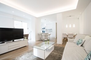 Una sala de estar moderna con un televisor de pantalla plana, una mesa de centro de vidrio, un sofá y una zona de comedor con sillas y una mesa.