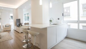 A modern kitchen with white cabinetry, a large island with bar stools, and a window providing natural light. - Spacious 4BR Apartment, Walk to Beach (Alacant)