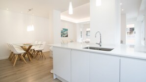 A modern kitchen with white cabinetry, a central island with a sink, and pendant lighting. - Spacious 4BR Apartment, Walk to Beach (Alacant)