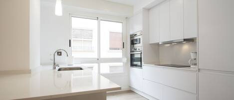 A modern kitchen with white cabinetry, a built-in oven, and a large window providing natural light.