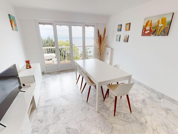 A modern dining area with a white table and chairs, a balcony with a view, and artwork on the walls.