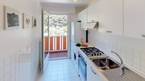 A narrow kitchen with white cabinets, a gas stove, and a sink. - Top-floor 2-room with air con & private parking in Menton (Menton)