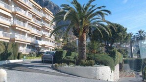 A multi-story hotel with balconies, palm trees, and a mountainous backdrop. - Top-floor 2-room with air con & private parking in Menton (Menton)