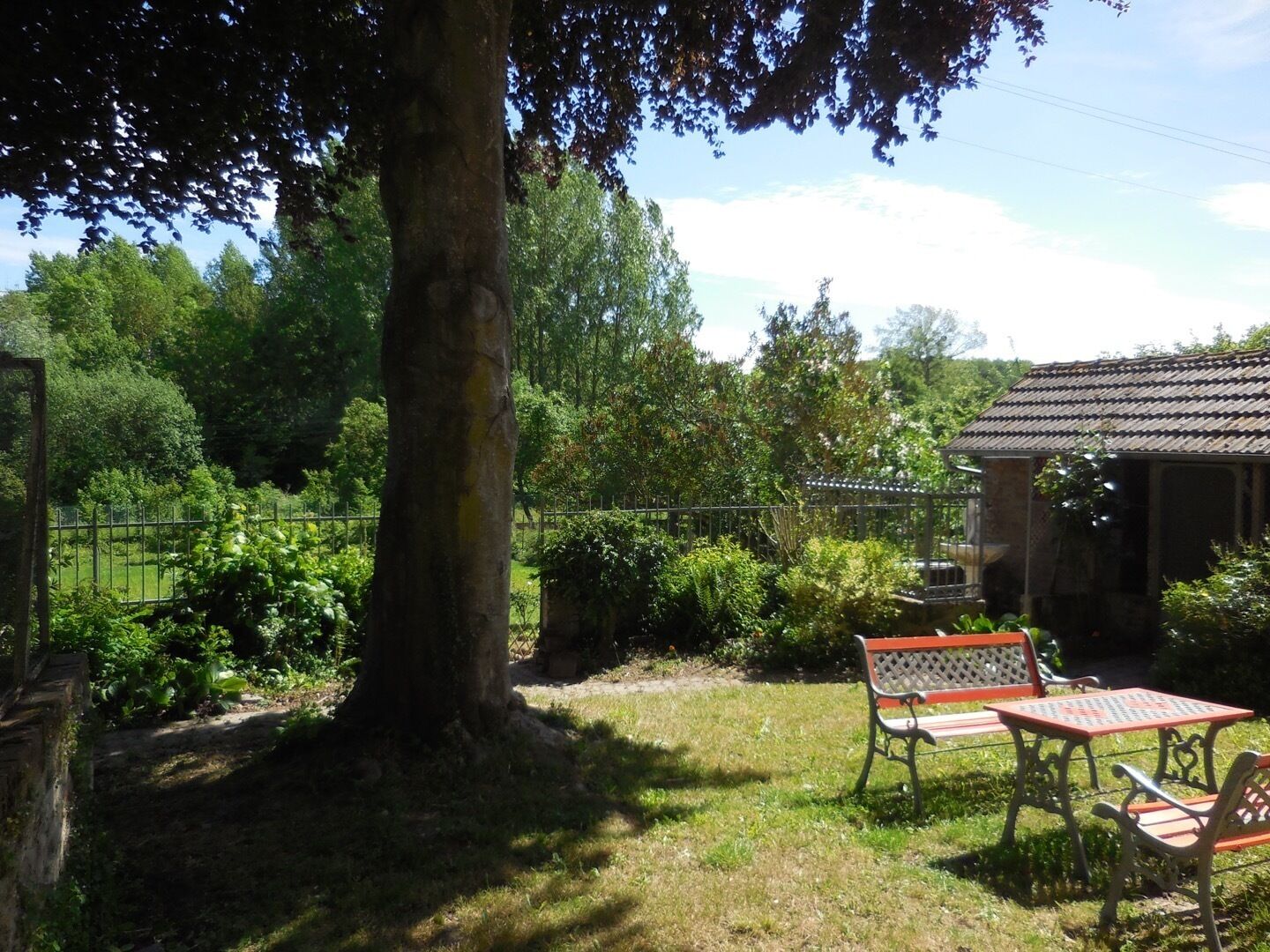 A garden with a large tree, a wooden structure, and two metal tables with benches.