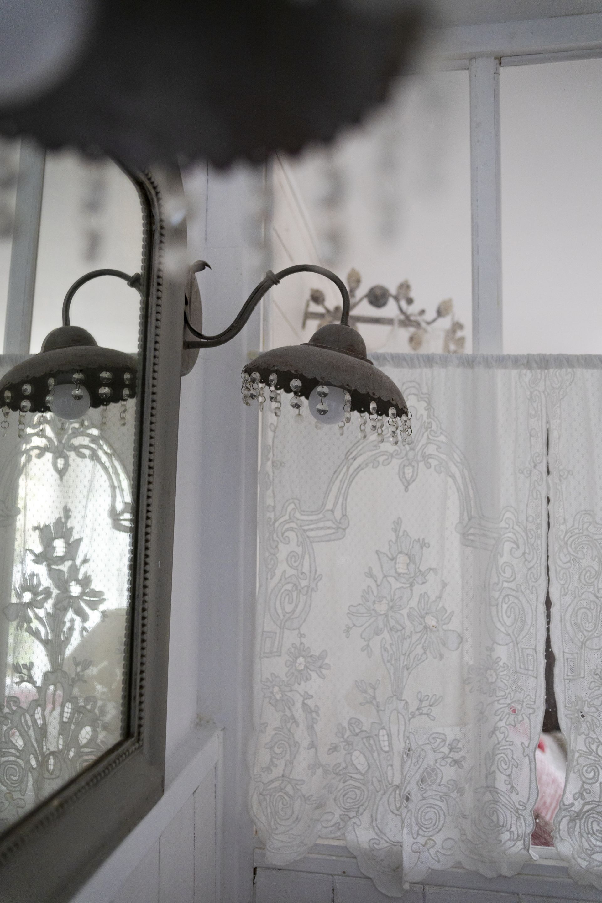A room with a mirror, a decorative light fixture, and a window with a floral curtain.