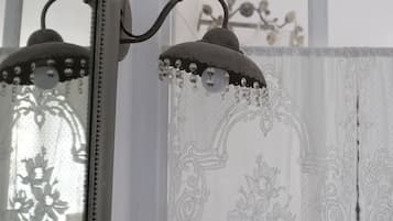 Une pièce avec un miroir, un luminaire décoratif et une fenêtre ornée d’un rideau à motifs floraux.
