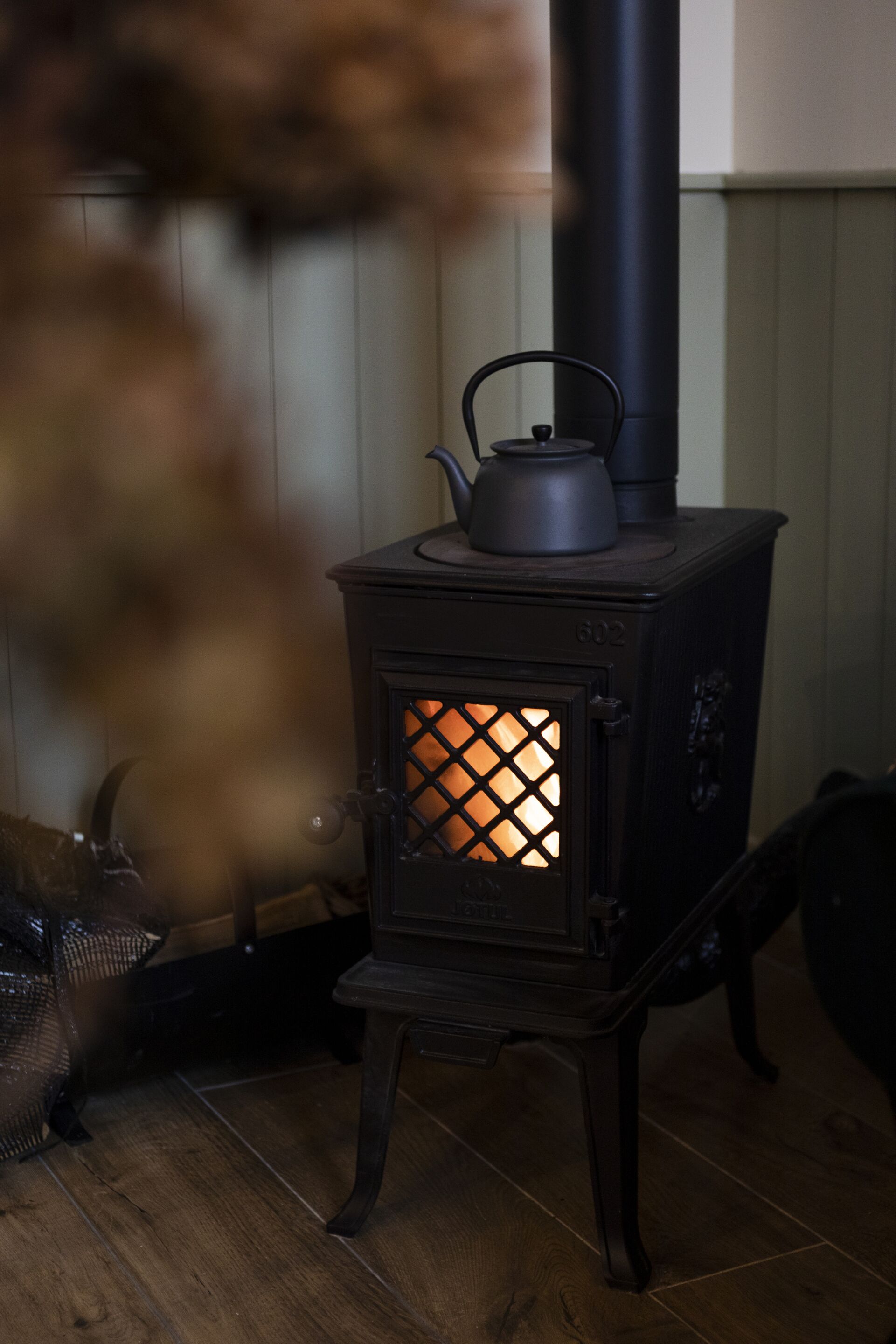 A wood-burning stove with a visible fire, a kettle on top, and a chimney.