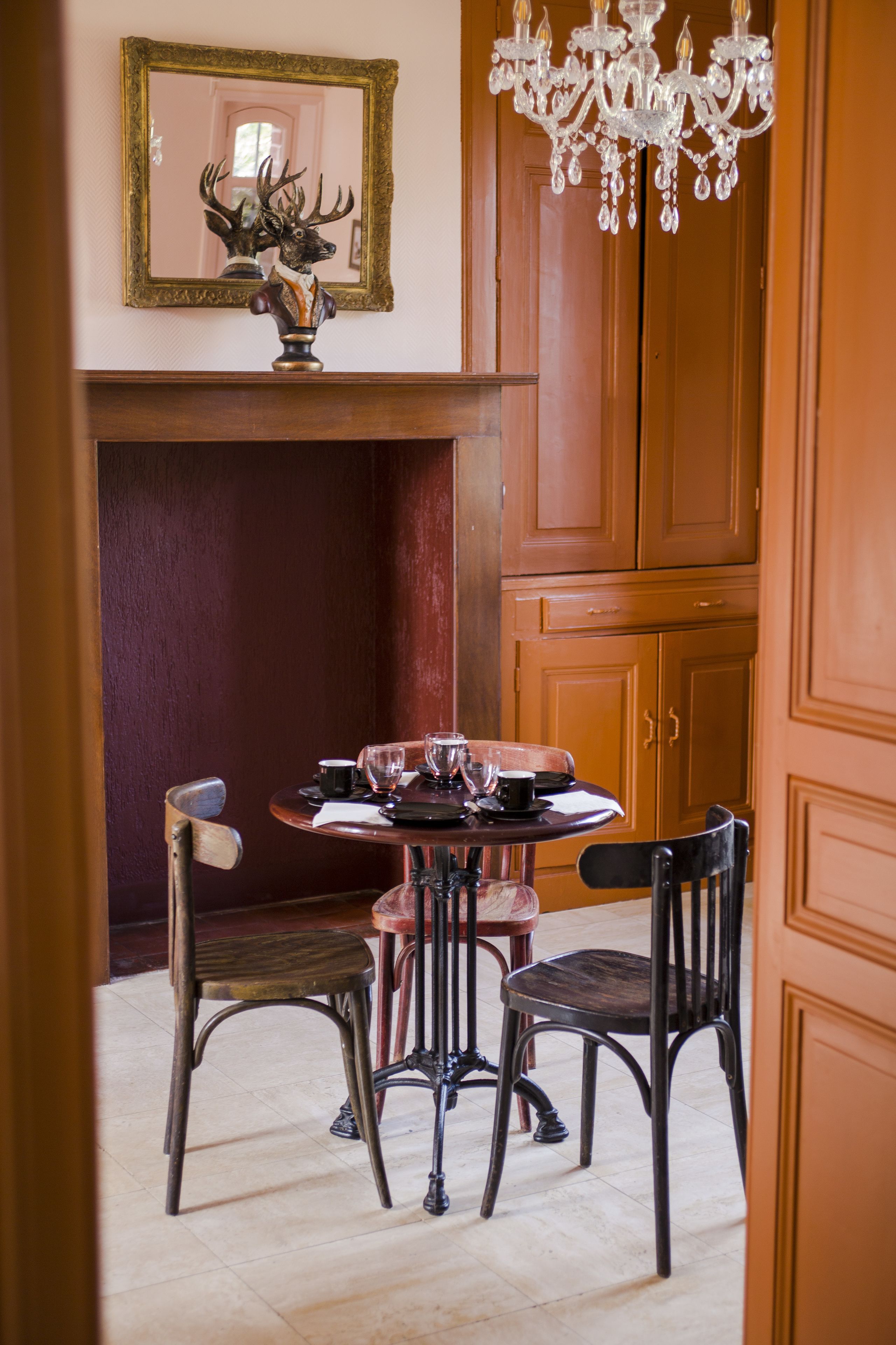 A dining area with a wooden table, four chairs, a chandelier, and a mirror on the wall.