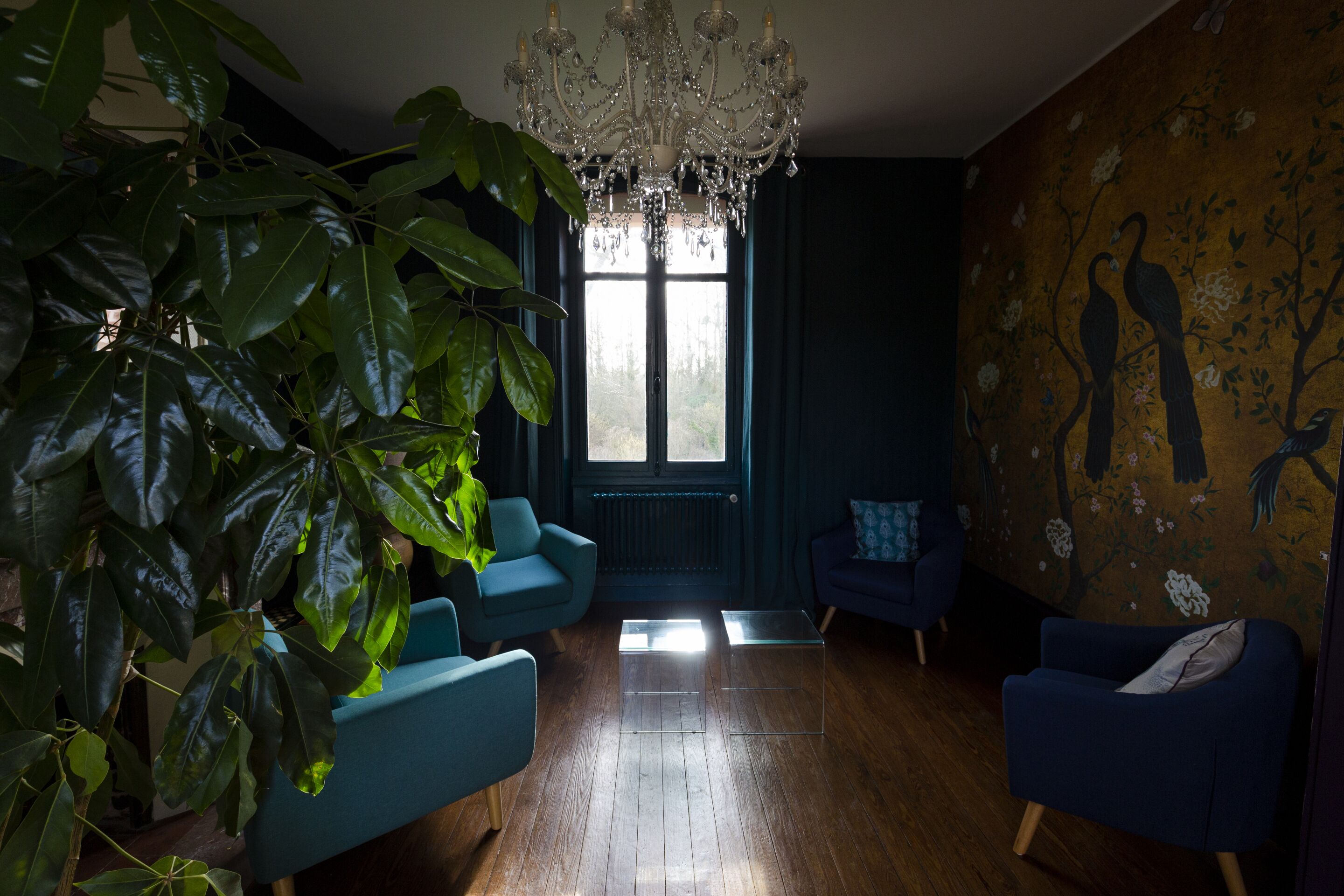 A room with a large window, a chandelier, and a wall with a bird mural.