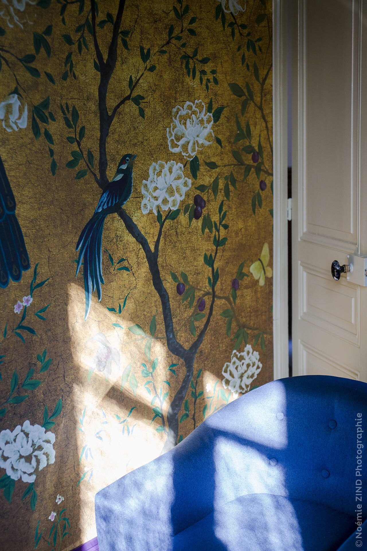 A room with a mural of a bird on a tree branch, a white door, and a blue sofa.