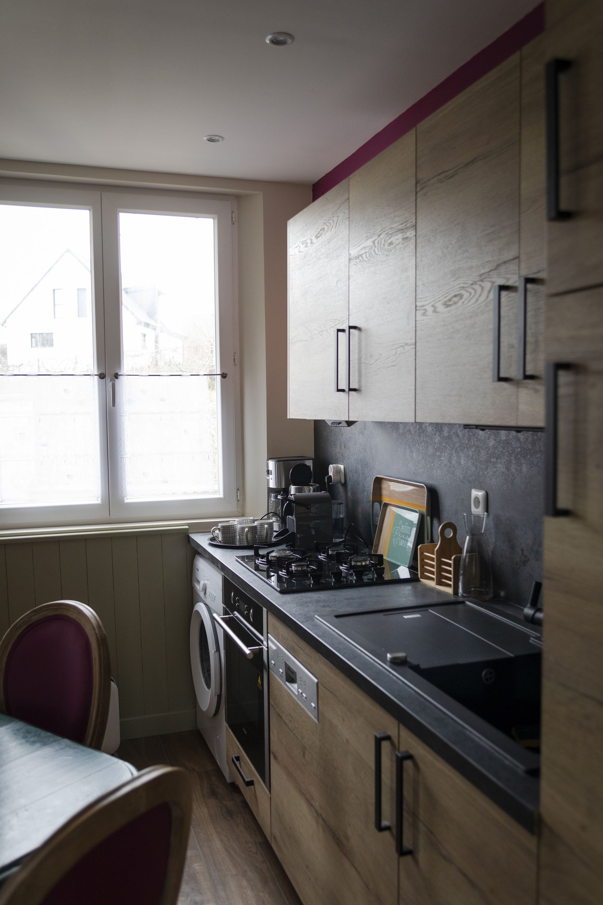 Une cuisine compacte équipée d’un lave-linge, d’une machine à café et d’un coin repas avec une table et des chaises.