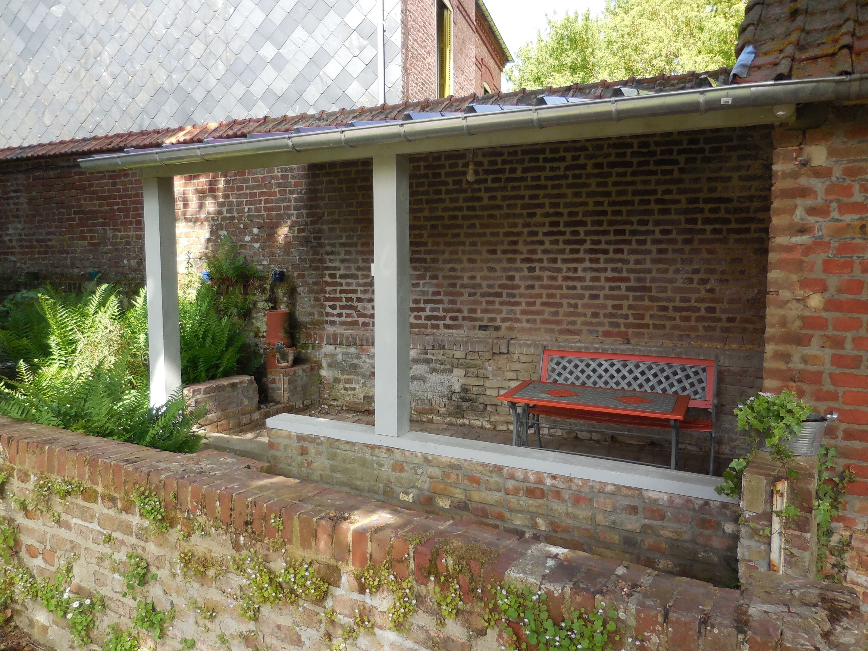 A brick building with a covered porch, a bench, and potted plants.
