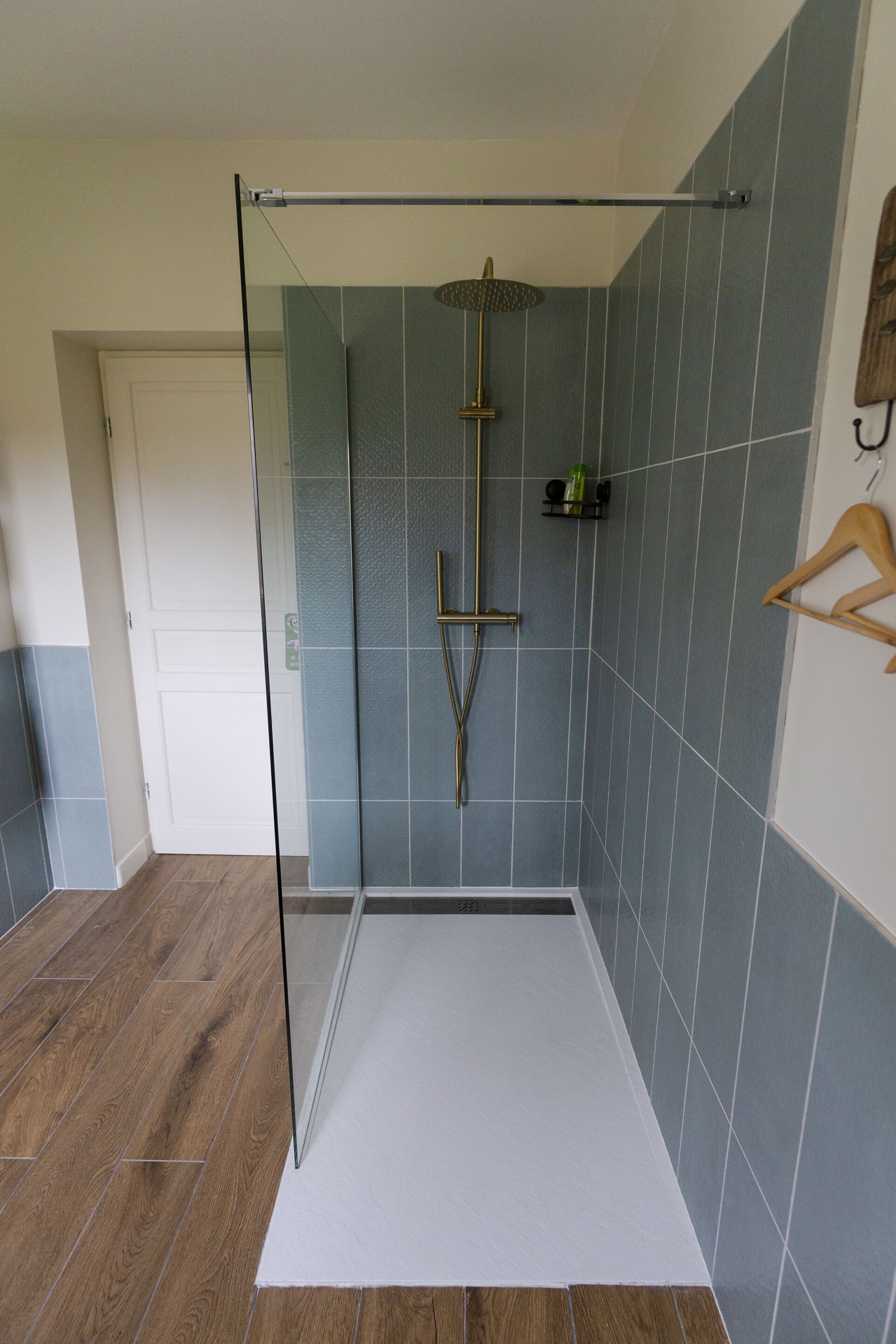 A modern bathroom with a glass shower enclosure, wooden flooring, and blue-tiled walls.