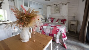 Een slaapkamer met een houten bed, een witte nachtkastje, een bijzettafeltje met een vaas, en een raam met gordijnen.